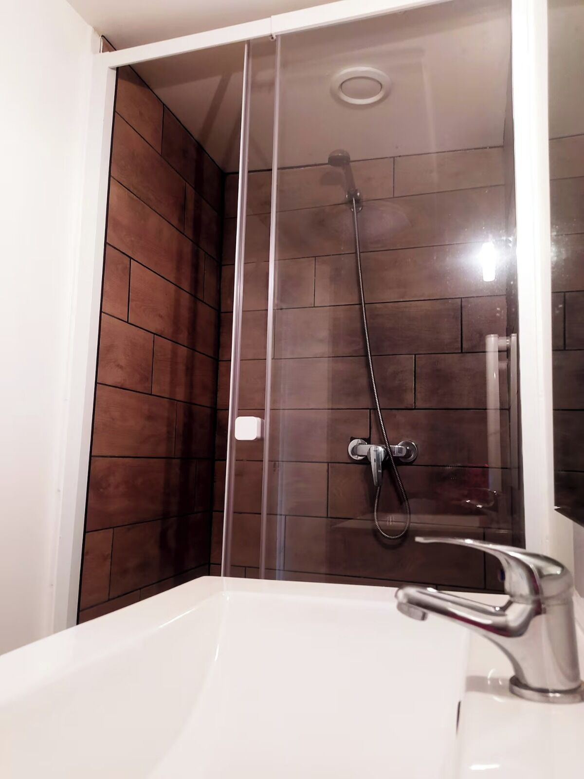 A modern bathroom with a glass-enclosed shower, a white sink, and dark brown tiled walls.