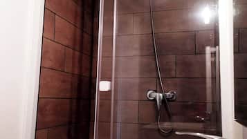 A modern bathroom with a glass-enclosed shower, a white sink, and dark brown tiled walls.