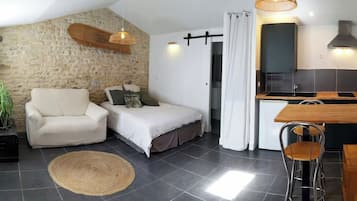 A compact room with a bed, a chair, a small kitchenette, and a stone wall.