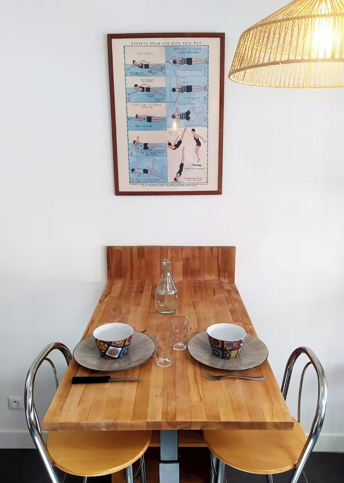 A dining table with two chairs, a framed instructional poster, and a hanging light fixture.