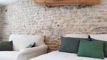 A bedroom with a stone wall, a bed with white bedding, and a wooden surfboard mounted on the wall.