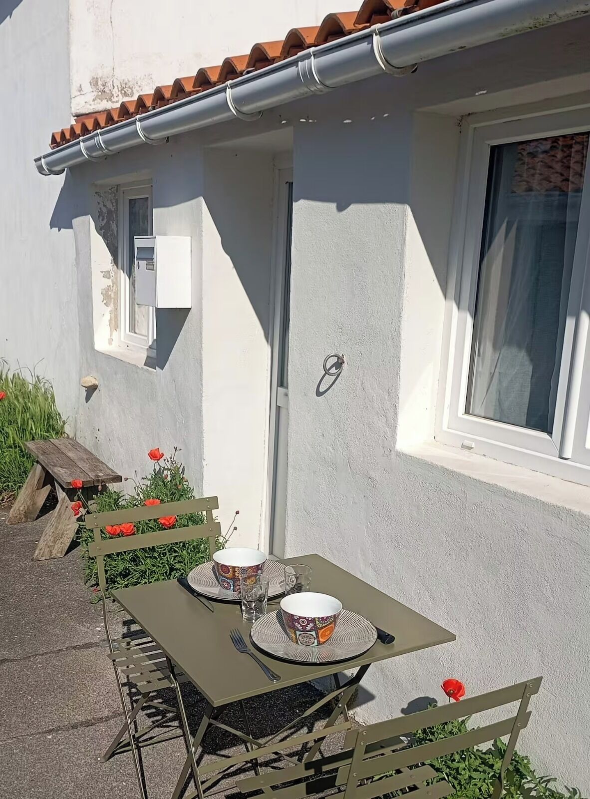 Un espace extérieur aménagé pour prendre les repas, avec une table et des chaises, une fenêtre et une porte sur un bâtiment.