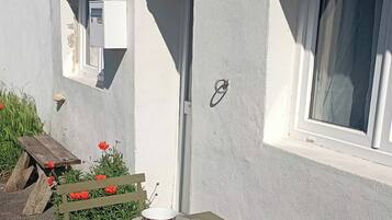 Un espace extérieur aménagé pour prendre les repas, avec une table et des chaises, une fenêtre et une porte sur un bâtiment.