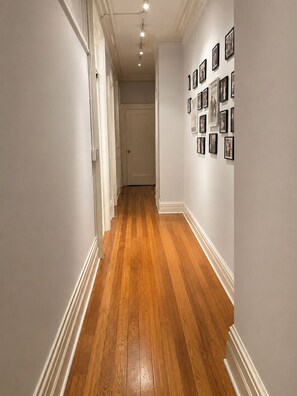 A hallway with wooden flooring, white walls, and framed pictures on the right wall. - 3-bedroom sleeps up to 5 apartment in charming NYC by Central Park (New York)