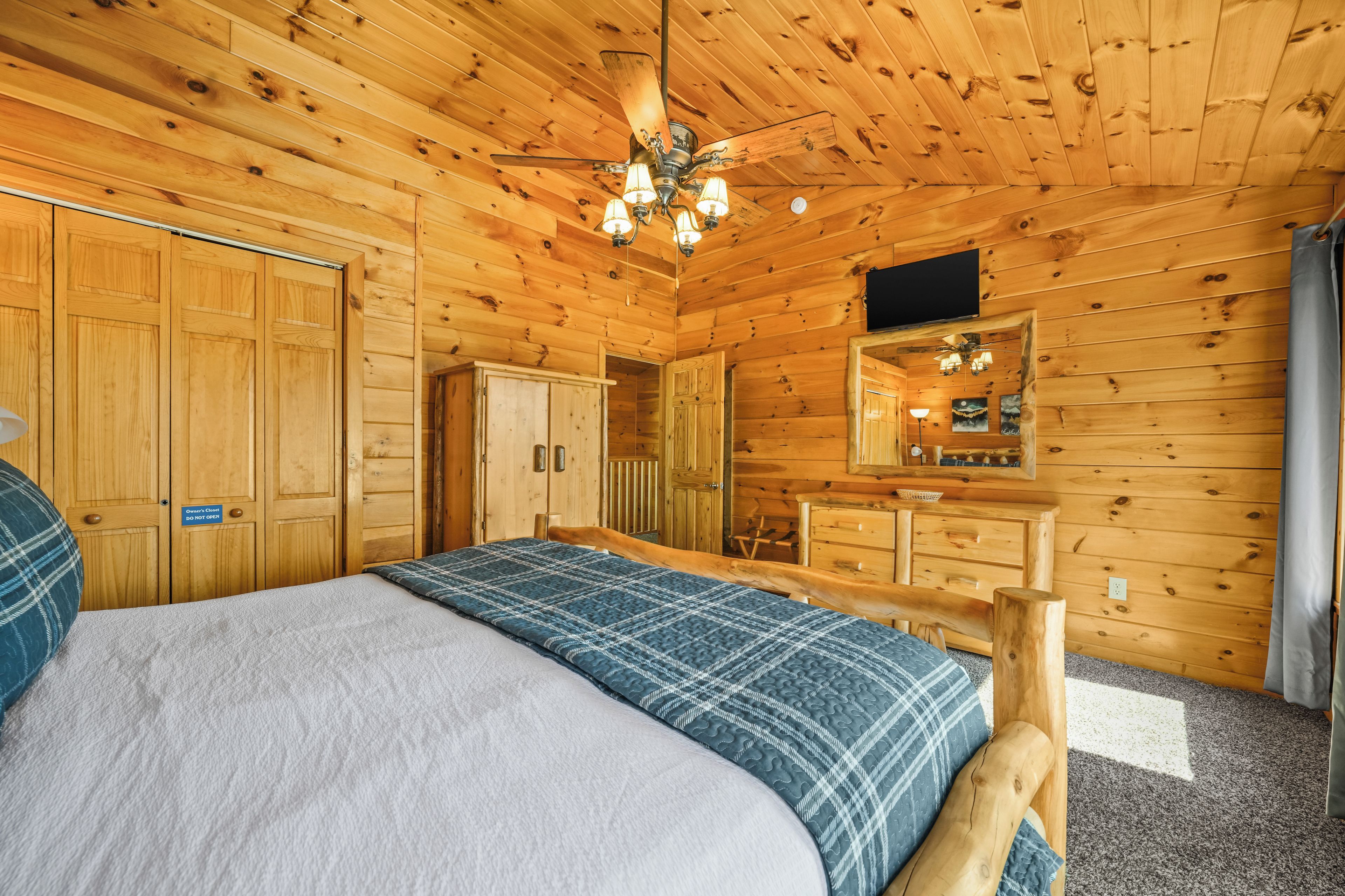 A wooden cabin room with a bed, a wardrobe, a mirror, and a ceiling fan.