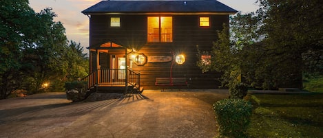 A two-story log cabin with a porch and a driveway leading to the entrance.