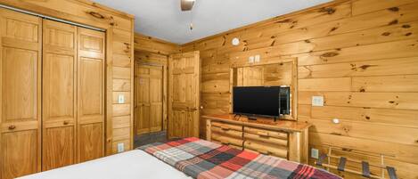 Une chambre dans un chalet en bois, équipée d’un lit, d’une télévision et d’un ventilateur de plafond.