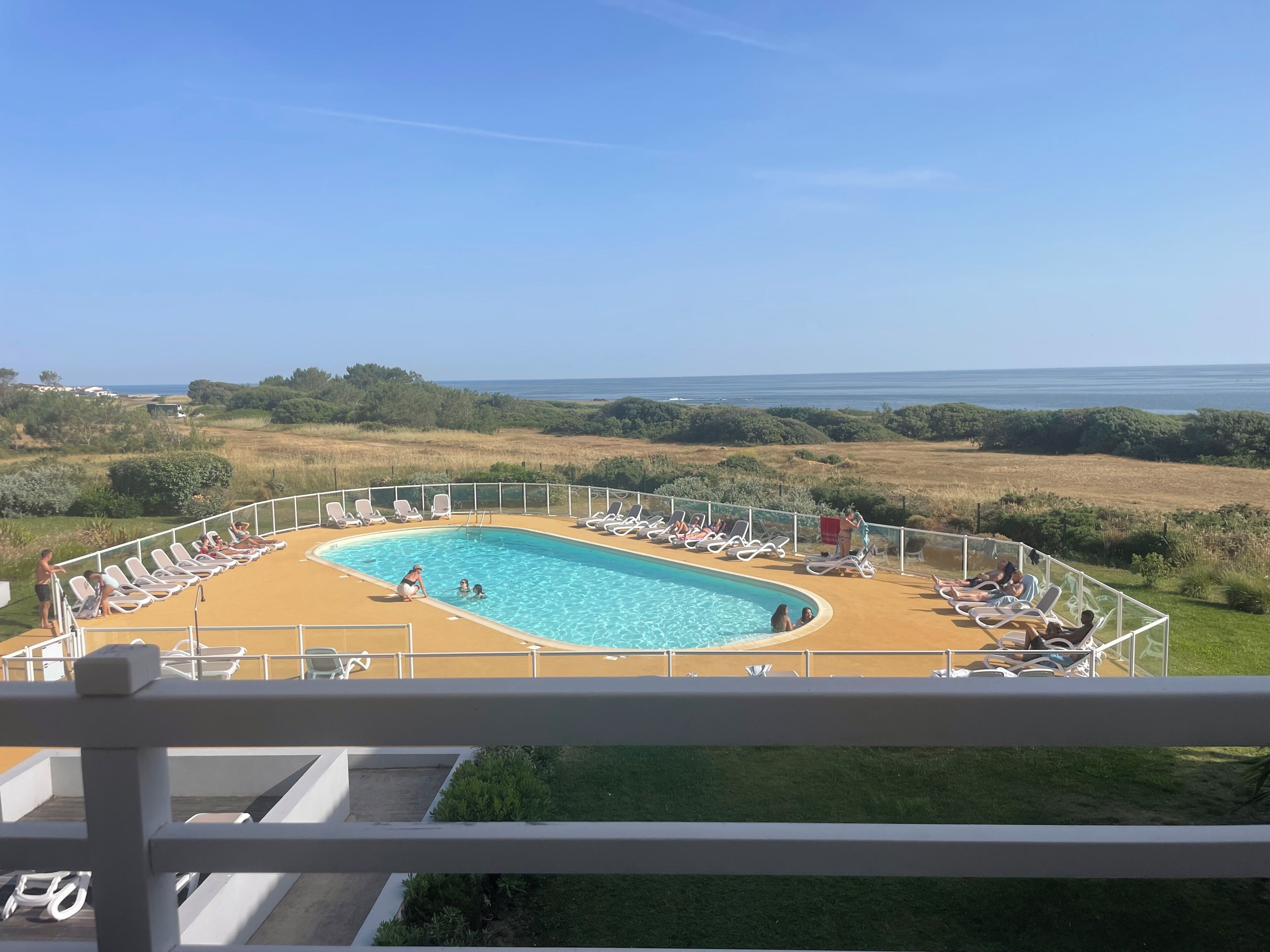 A pool area with a view of the sea, surrounded by lounge chairs and a fenced deck.