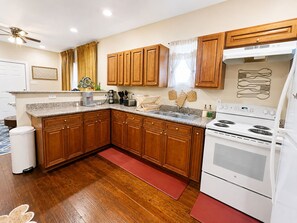 A kitchen with wooden cabinets, a white stove, and a red rug. - NOLA Boho Duplex , 2BR • Near LSUNO • 10 Min to Downtown (New Orleans)