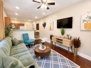 A living room with a sofa, a blue chair, a coffee table, a TV, and a ceiling fan.