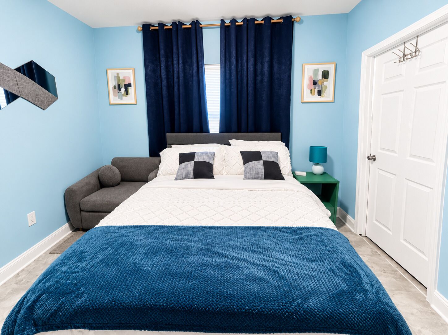 A bedroom with a bed, a nightstand, a chair, a door, and two framed pictures on the wall.