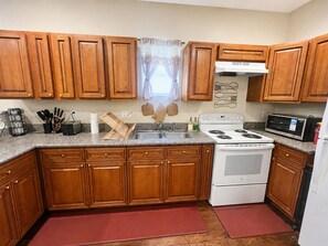 A kitchen with wooden cabinets, a white stove, a microwave, and a sink. - NOLA Boho Duplex , 2BR • Near LSUNO • 10 Min to Downtown (New Orleans)