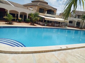 A swimming pool with a tiled edge, surrounded by a patio area with outdoor seating and palm trees. - Beautiful private villa in a gated community with a garden—centrally located, with everything within walking distance! (Saly)