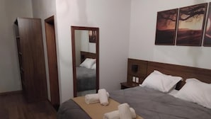 A hotel room with a bed, a wooden wardrobe, a mirror, and artwork on the wall.