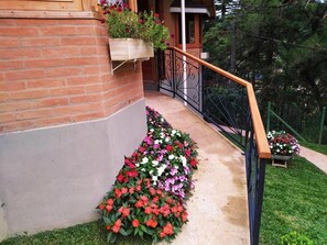 A brick building with a wooden staircase, a metal railing, and a flower bed with red and white flowers. - POUSADA ALTO DOS PINHEIROS (Camanducaia)