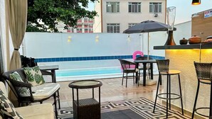 Une terrasse avec piscine, des espaces de détente en plein air et un coin bar.