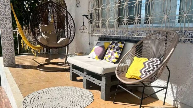 A sunlit patio with a hammock, a cushioned seating area, and a decorative wall.