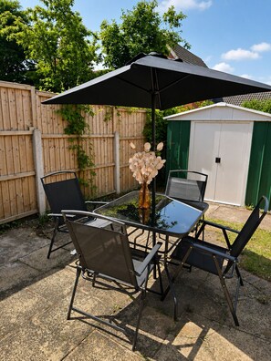Eine Terrasse im Freien mit Tisch, Stühlen, einem großen Sonnenschirm und einer Vase mit Blumen.