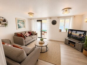 Ein Wohnzimmer mit Sofa, Couchtisch, Fernseher und Blick durch eine Glastür.