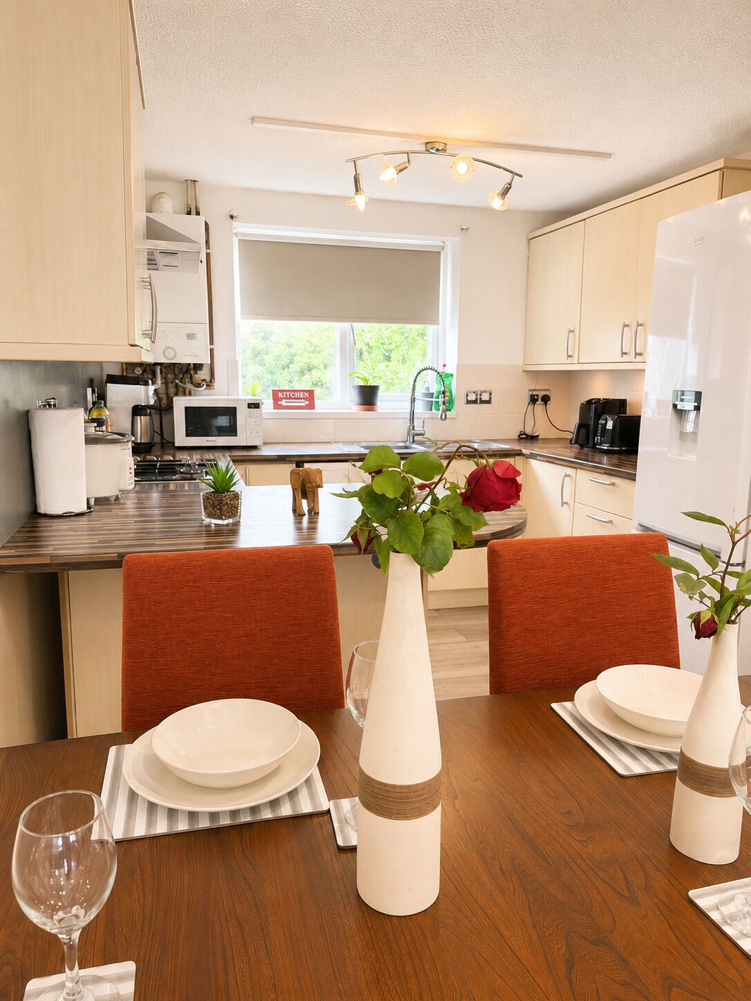 A modern kitchen with white cabinets, a dining table set with plates, a vase with a plant, and a wine glass.