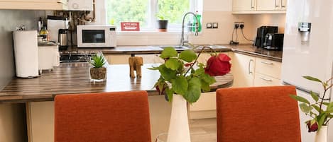 A modern kitchen with white cabinets, a dining table set with plates, a vase with a plant, and a wine glass.