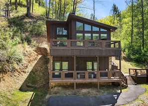 Eine zweistöckige Holzhütte mit einem Balkon, umgeben von einem bewaldeten Hügelhang.