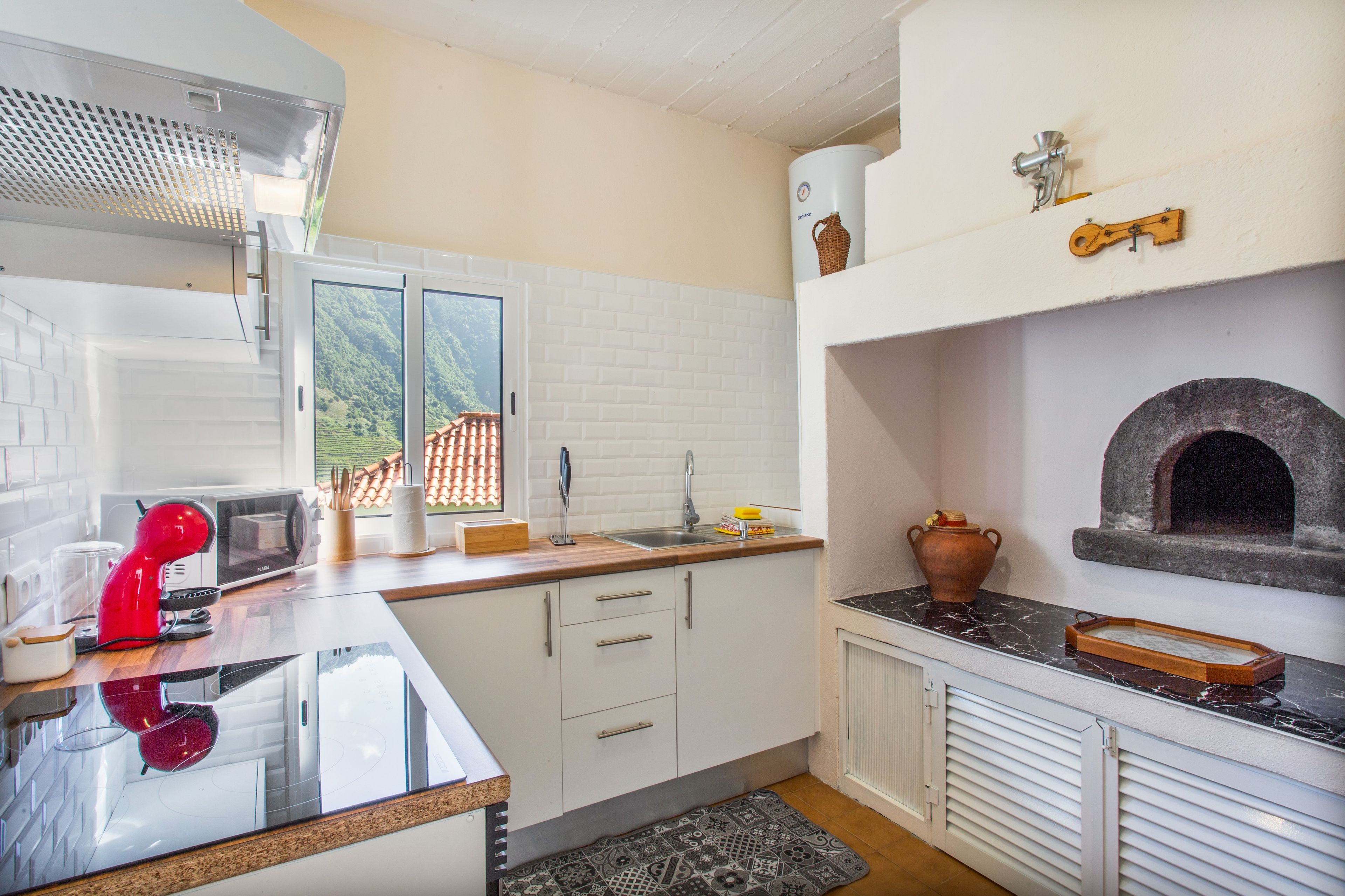 A kitchen with white cabinets, a red mixer, a microwave, a sink, and a stone oven.