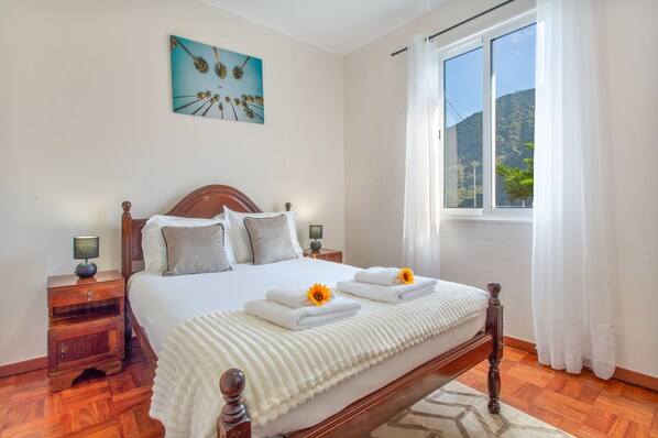 A neatly made bed with white linens, a wooden headboard, and two bedside tables with lamps.