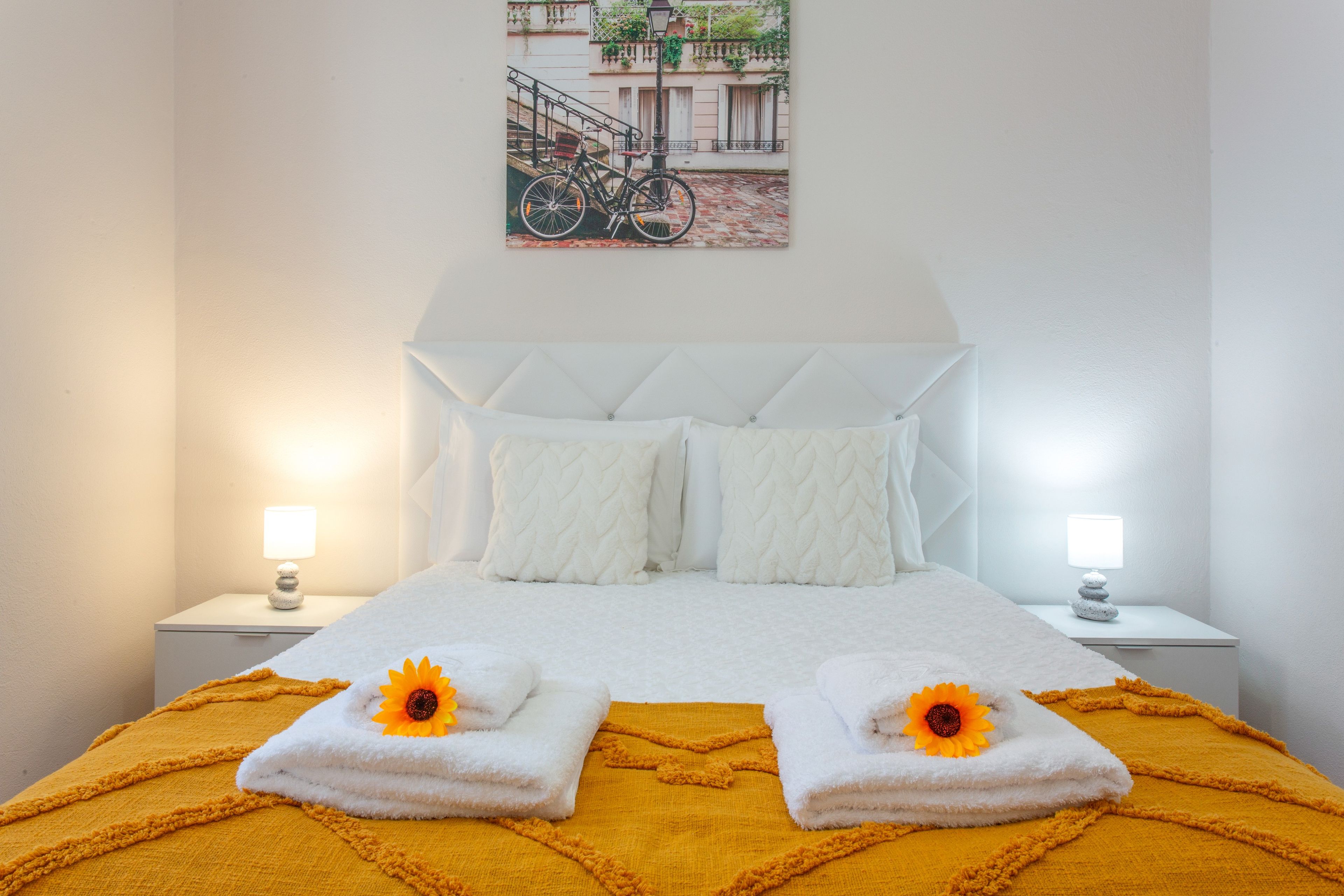 Ein Hotelzimmer mit einem großen Bett, weißer Bettwäsche, zwei Nachttischen mit Lampen und einem Wandbild eines Fahrrads.