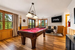 A pool table in a room with large windows, a sofa, and a television screen displaying the word 'chody'. - Mountain Escape - Hot Tub - Game Room - Sleeps 8 (Pigeon Forge)