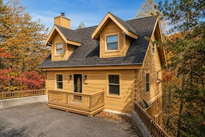 A two-story wooden cabin with a porch, a chimney, and a fenced driveway. - Mountain Escape - Hot Tub - Game Room - Sleeps 8 (Pigeon Forge)