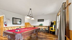 Ein Billardtisch mit roter Spieltuchoberfläche, Holzboden und einem Schild mit der Aufschrift ‚Spielraum‘ an der Wand.