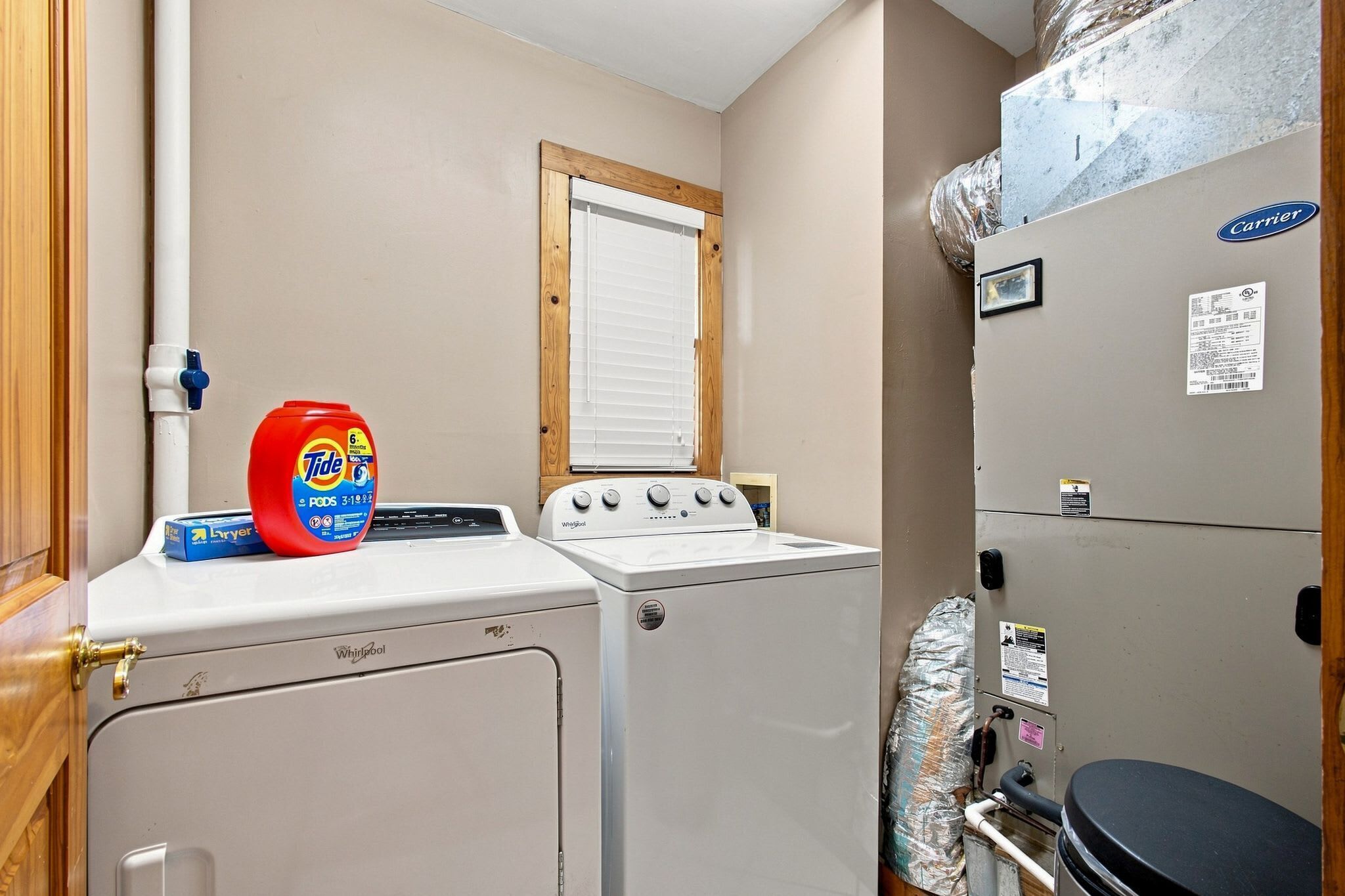 A laundry room with a Whirlpool washer and dryer, a Tide detergent bottle, and a Carrier refrigerator.