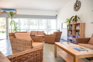 A spacious room with wicker furniture, a wooden coffee table, and a bookshelf. - T2 près de la plage | Piscine sur place | Terrasse (Le Verdon-sur- Mer)