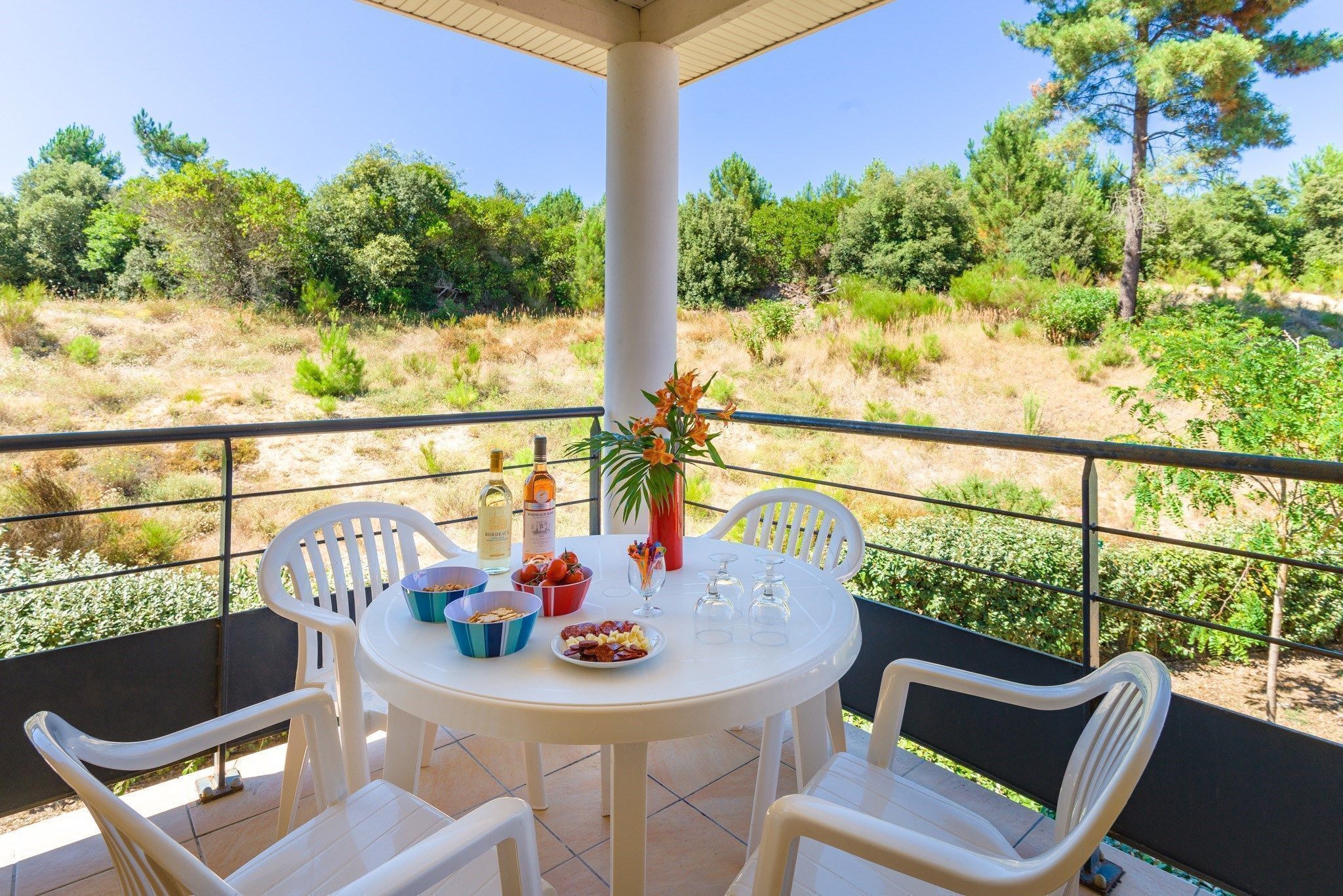 A round table with chairs on a balcony, a vase with flowers, and a bottle of wine.