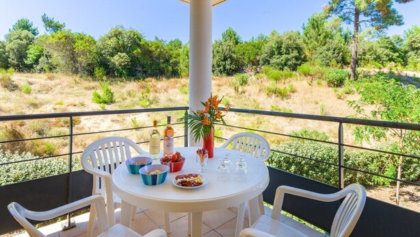 Een ronde tafel met stoelen op een balkon, een vaas met bloemen en een fles wijn.
