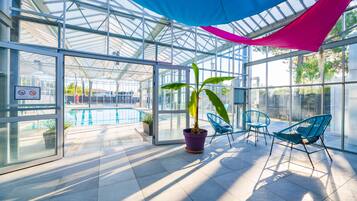 Et glasindhegnet område med pool, stole og potteplanter.