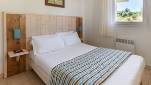 A bedroom with a wooden headboard, a bed with white linens, a striped blanket, a nightstand with a book, and a window with a view of greenery.