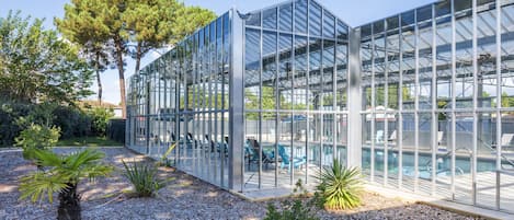 Une serre moderne en verre, avec un espace piscine visible à travers les parois transparentes.