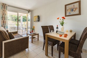 Un coin repas avec des chaises en osier, une table en bois et une vue sur une terrasse extérieure, accessible par une porte vitrée.