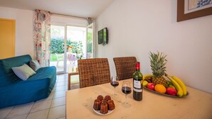 A dining area with a table set for two, featuring a bottle of wine, glasses, and a fruit bowl.