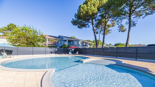A swimming pool with a curved design, surrounded by a tiled deck and a fence.