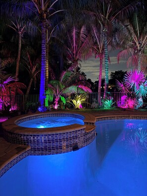 A swimming pool surrounded by palm trees and tropical plants, illuminated with colorful lights. - Private Waterfront Retreat with Pool- Fort Lauderdale 10 min from beaches (Wilton Manors)