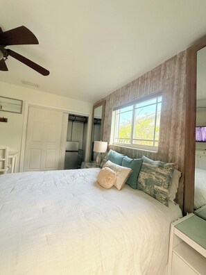 A bedroom with a large bed, a ceiling fan, a window with curtains, and a door. - Private Waterfront Retreat with Pool- Fort Lauderdale 10 min from beaches (Wilton Manors)