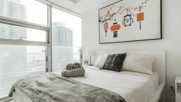 Een moderne hotelkamer met een groot raam, een net opgemaakt bed, een decoratief wandobject en een nachtkastje met een lamp.
