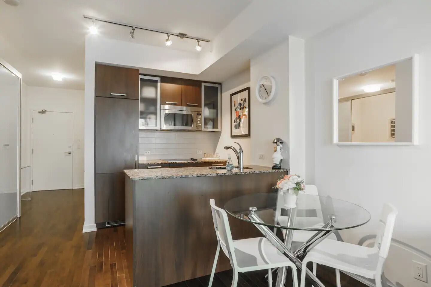 A modern kitchen with a central island, stainless steel appliances, and a dining area with a glass table and white chairs.