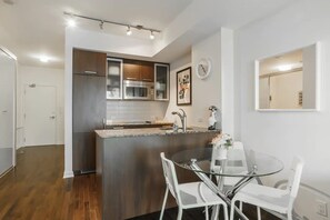 Una cocina moderna con una isla central, electrodomésticos de acero inoxidable y un comedor con mesa de vidrio y sillas blancas.