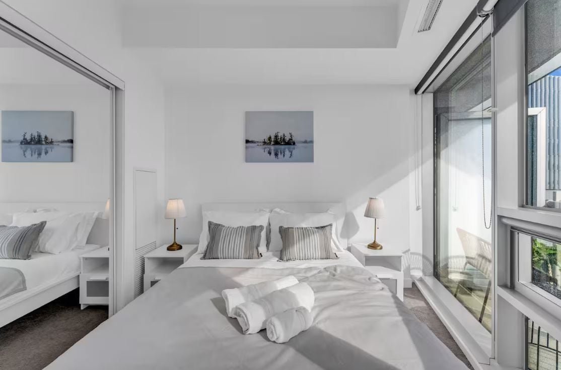 A modern hotel room with a large bed, two bedside tables, a window with a view, and two wall-mounted paintings.