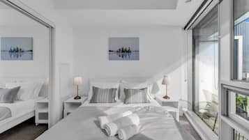 A modern hotel room with a large bed, two bedside tables, a window with a view, and two wall-mounted paintings.