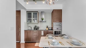 A modern kitchen with wooden cabinets, a built-in oven, and a dining area with a table set for four. - Harbour Skyline (Toronto)